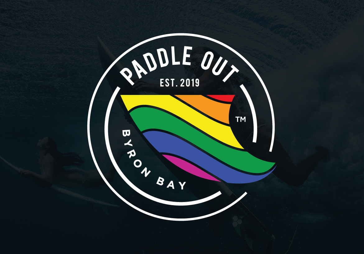 Official circular badge logo for Paddle Out, established in 2019 in Byron Bay, featuring the iconic rainbow shark fin design.